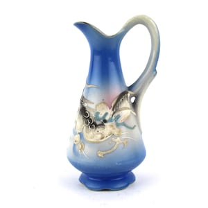 Op de afbeelding: Een kleine blauwe keramische kan met een drakenontwerp. De kan heeft een handvat en een tuit. De draak is geschilderd in goud, zwart en wit.