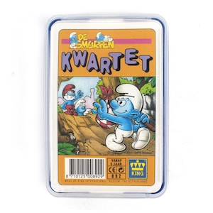 May include: A Smurfs Kwartet card game in a clear plastic case. The card features Smurf characters in a forest scene with the text "DE SMURFEN KWARTET". The card is from 1994 and made by King International.