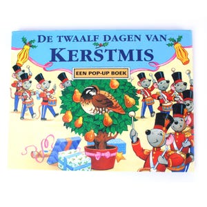 Peut inclure: Un livre pop-up intitulé DE TWAALF DAGEN VAN KERSTMIS illustré avec un poirier en pot central et un oiseau dans les branches. La scène est entourée de souris de dessin animé vêtues d'uniformes militaires rouges et bleus jouant du tambour.