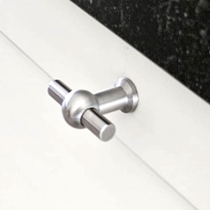 Könnte beinhalten: Nahaufnahme eines modernen Schrankknaufs aus gebürstetem Metall. Der Knauf hat einen zylindrischen Griff, eine kugelförmige Mitte und eine kreisförmige Basis. Die Hardware ist auf einer weißen Oberfläche mit dunklem, strukturiertem Hintergrund montiert.