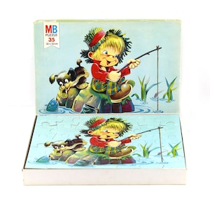 Può includere: Una scatola di puzzle vintage MB con un'illustrazione colorata di un bambino che pesca con un cane al suo fianco. La scatola del puzzle è etichettata "MB Puzzle 35 32 x 22cm".