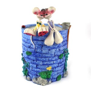 May include: A whimsical blue ceramic well planter with a brick design, adorned with green foliage and a yellow flower. Two cartoon mice figures are perched on the edge, one with red polka-dot shoes. A small bucket is visible.