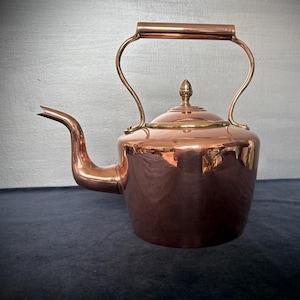 May include: A copper kettle with a curved spout and a brass handle. The kettle has a rounded body and a lid with a decorative finial. The copper surface reflects light, creating a warm aesthetic. A classic kitchenware item.