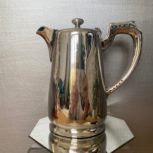 May include: A silver teapot with a polished finish and a rounded body. The teapot has a spout and a handle with a decorative design.