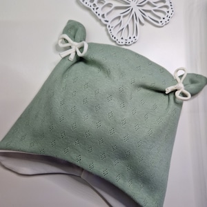 Op de afbeelding: Een saliegroene gebreide baby muts met witte banden. De muts heeft een witte voering en een ruitpatroon.