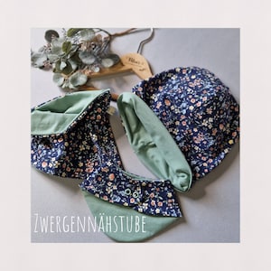 Pode incluir: Um conjunto de acessórios para bebé com padrão floral. O conjunto inclui um chapéu e um babador. O chapéu é feito de um material macio e elástico e tem um padrão floral. O babador é feito de um material semelhante e tem um padrão floral com fecho de botão. O conjunto é num esquema de cores azul e verde.