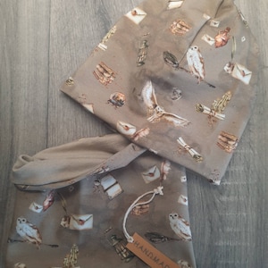 Puede incluir: Un gorro de punto beige y un cuello de punto a juego con un patrón de búho marrón y letras. La etiqueta dice "HANDMADE".