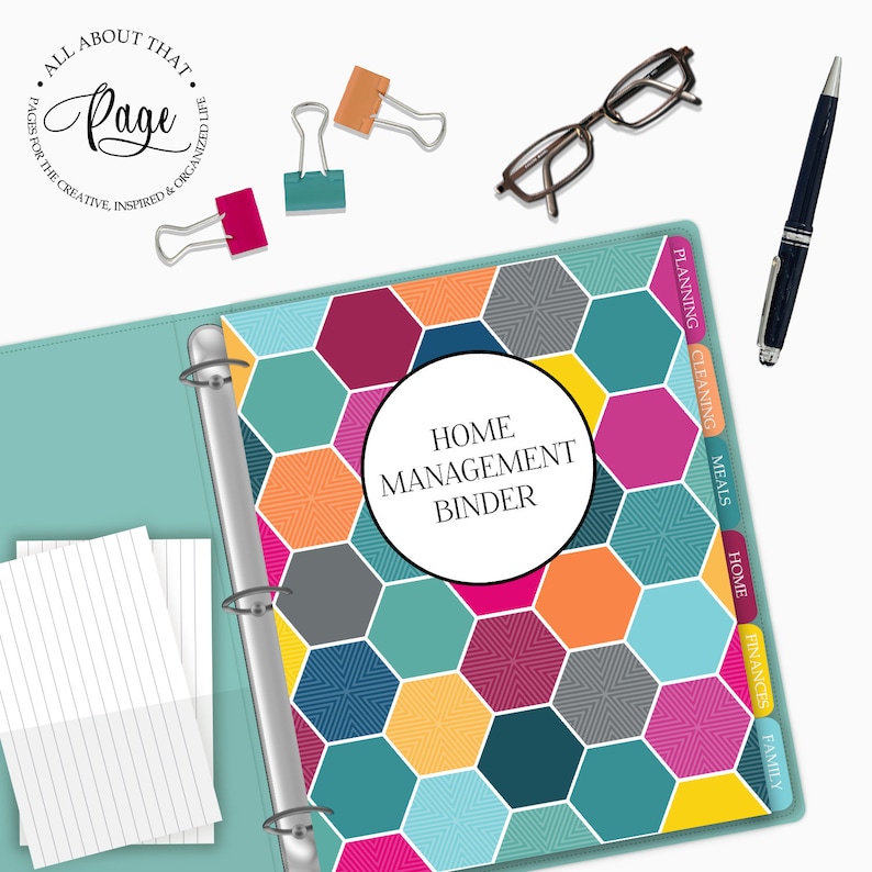 May include: A teal binder with a colorful geometric pattern on the cover. The binder has a silver ring mechanism and tabs labeled "Family", "Finances", "Home", "Meals", "Cleaning", and "Planning". The text "HOME MANAGEMENT BINDER" is printed in a white circle on the cover.