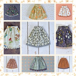 May include: A collage of nine doll skirts in various patterns and colors. The skirts feature floral, mushroom, and pumpkin designs. Each skirt has a lace trim at the hem. Colors include green, orange, brown, and white.