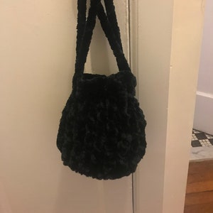 May include: A small black fuzzy bucket bag with a drawstring closure and two black straps.