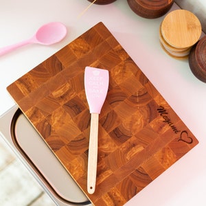 May include: A wooden cutting board with a pink spatula that says "Keep Calm and Bake On". The board is engraved with the name "Megan" and a heart.