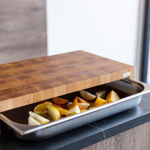 May include: A wooden cutting board with a built-in stainless steel tray. The tray is filled with sliced fruit, including pears, oranges, and persimmons.