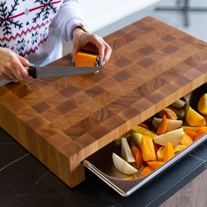 May include: A wooden cutting board with a built-in drawer. The drawer is open and contains sliced fruit, including oranges, pears, and persimmons.