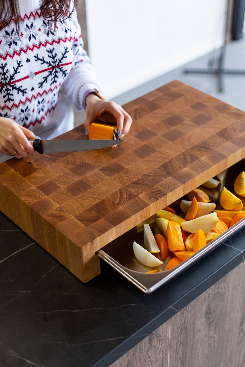 May include: A wooden cutting board with a built-in drawer. The drawer is open and contains sliced fruit, including oranges, pears, and persimmons.