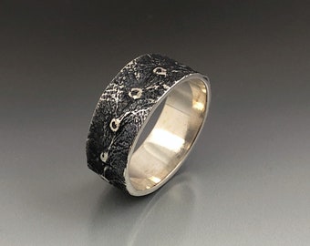 May include: A silver band ring with a textured black finish and a row of small white dots.