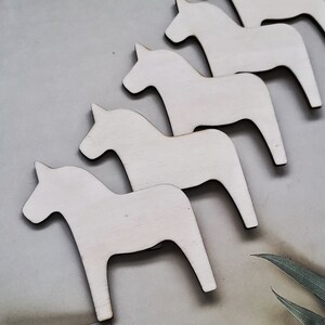 May include: Five white wooden horses, also known as Dala horses, are arranged in a row. The horses are all facing the same direction and are all the same size. They are all painted white and have a simple, traditional design.