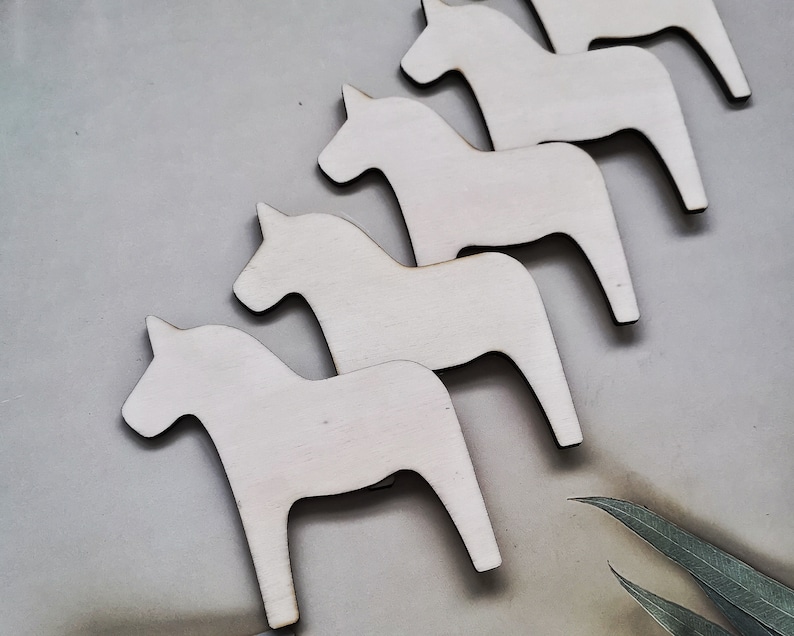 May include: Five white wooden horses, also known as Dala horses, are arranged in a row. The horses are all facing the same direction and are all the same size. They are all painted white and have a simple, traditional design.