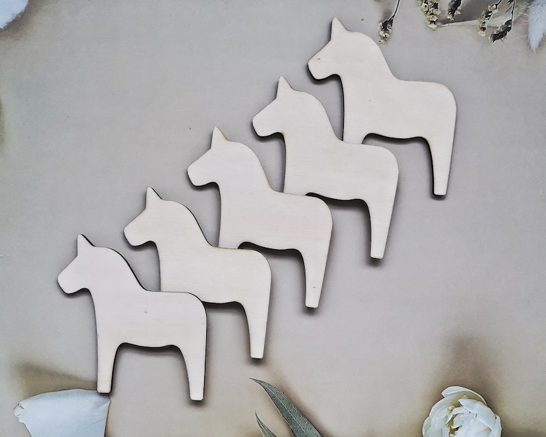 May include: Five unfinished wooden horse figurines in a row, all facing the same direction. The horses are all the same size and shape, and they are made of a light-colored wood.
