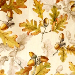 K&ouml;nnte beinhalten: Ein Textilstoff mit einem sich wiederholenden Muster aus Eichenbl&auml;ttern und Eicheln. Das Design umfasst leuchtend gelbe, orangefarbene und gr&uuml;ne Bl&auml;tter neben graut&ouml;nigen Bl&auml;ttern sowie goldbraune Eicheln auf einem cremefarbenen Hintergrund.