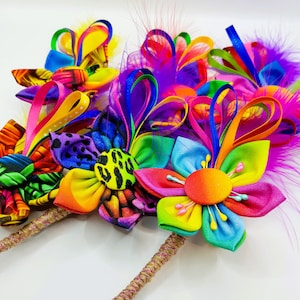 May include: A set of colorful fabric flower brooches with feathers and ribbons. The flowers are made of bright colors like pink, yellow, blue, green, and purple. The brooches are attached to a brown cord.