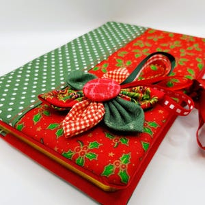 May include: A red and green fabric-covered journal with a holly pattern and a green and red fabric bow with a red button in the centre.