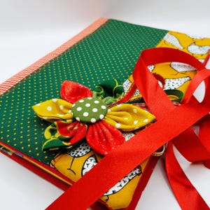 May include: A green and red fabric journal with a yellow and red flower embellishment and a red ribbon. The journal has a white polka dot pattern and a yellow fabric with a white chicken design.