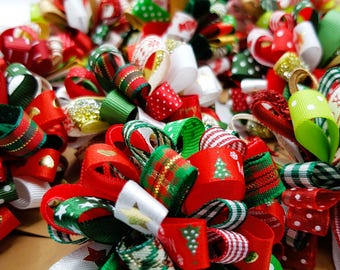May include: A close-up of a collection of Christmas-themed hair bows. The bows are made of red, green, and white ribbon with various patterns, including polka dots, stripes, and plaid. The bows are arranged in a cluster, creating a festive and colorful display.