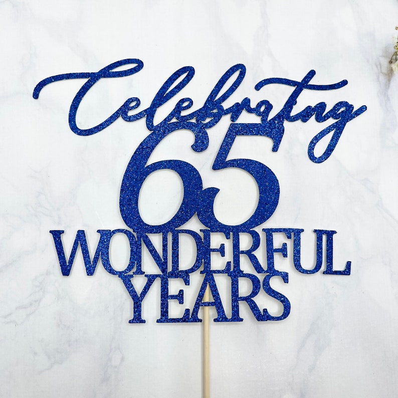 Może przedstawiać: Niebieski topper na ciasto z błyszczącymi drobinkami z napisem "Celebrating 65 Wonderful Years".