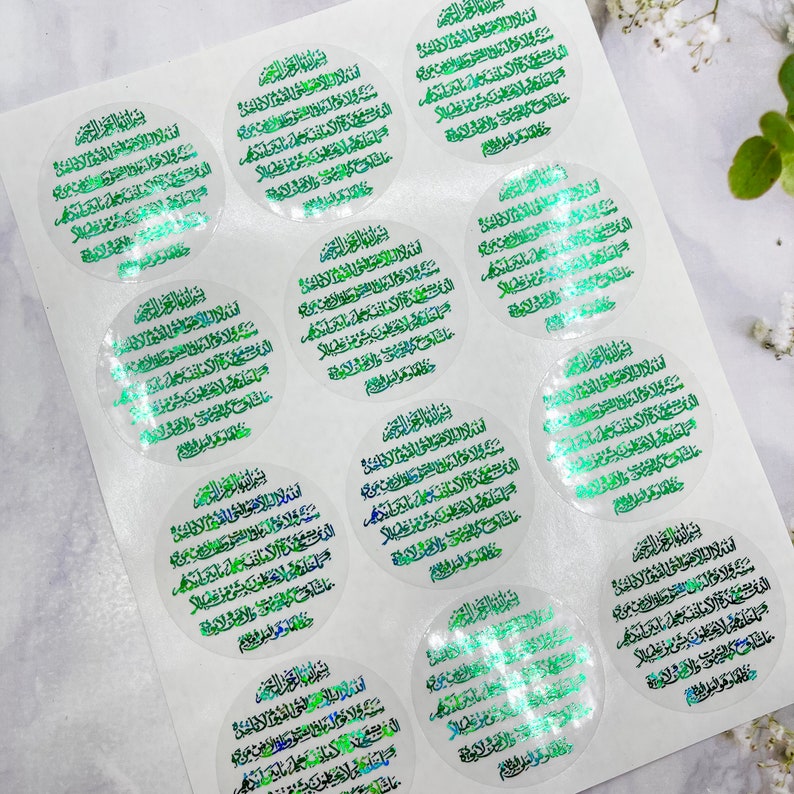 May include: A sheet of 12 round stickers with a green and white holographic design. The stickers feature Arabic text in a circular pattern.