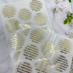 May include: A sheet of clear stickers with gold Arabic calligraphy. The stickers are round and have a white background. The calligraphy is in a traditional style and is very detailed.