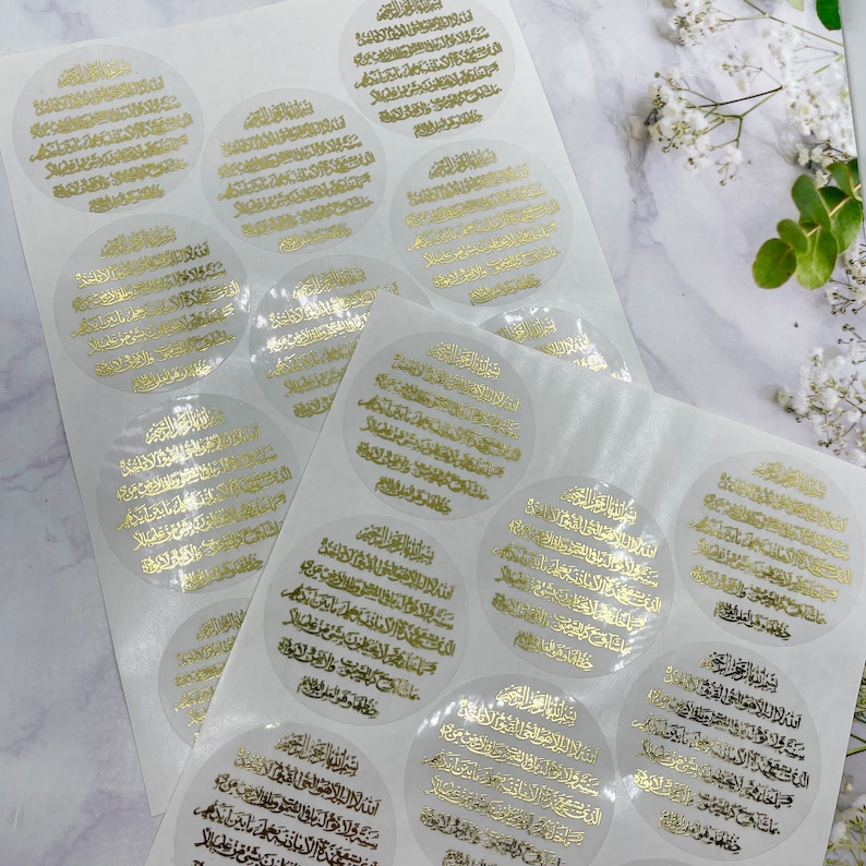 May include: A sheet of clear stickers with gold Arabic calligraphy. The stickers are round and have a white background. The calligraphy is in a traditional style and is very detailed.