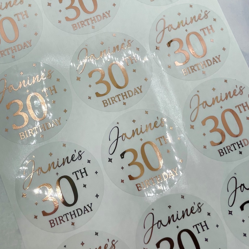 May include: A sheet of clear stickers with gold foil lettering. The stickers say "Janine's 30th Birthday".