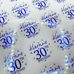 May include: Clear round stickers with blue text that says "Kieran's 30th Birthday".