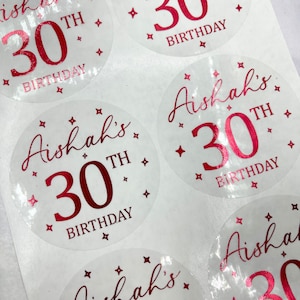 May include: Clear round stickers with pink text that says "Aishah's 30th Birthday" with a pink star design.