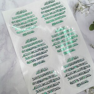 May include: A sheet of clear stickers with a circular design featuring Arabic text in green and gold foil. The text is a prayer or verse from the Quran.