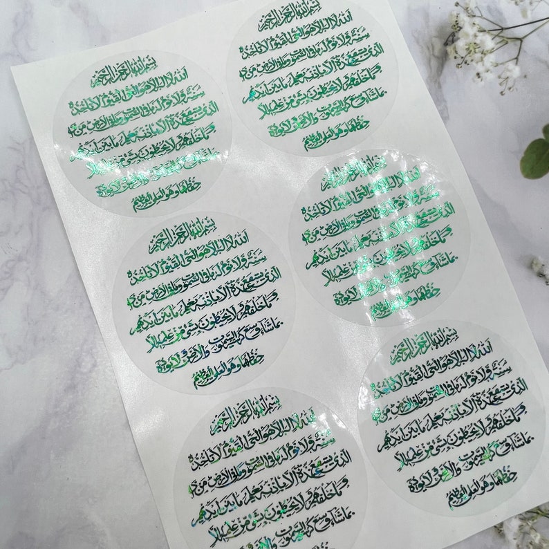 May include: A sheet of clear stickers with a circular design featuring Arabic text in green and gold foil. The text is a prayer or verse from the Quran.