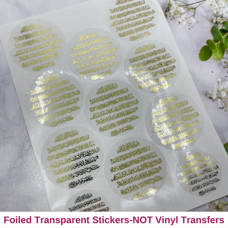 May include: A sheet of clear, transparent stickers with gold foil lettering. The stickers are round and feature Arabic script. The text on the stickers reads "Foiled Transparent Stickers-NOT Vinyl Transfers".