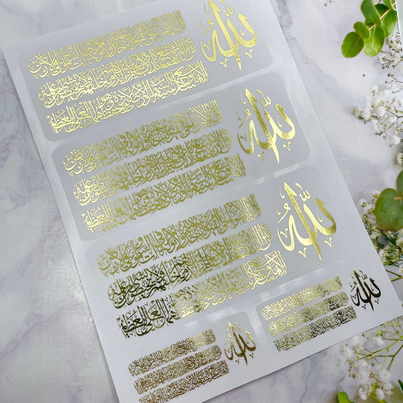 May include: A sheet of adhesive stickers featuring gold foil Arabic calligraphy. The design includes repeating rectangular blocks of intricate script alongside the word Allah in a stylized font. The stickers are arranged on a white backing.