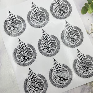 May include: A sheet of clear stickers featuring black Arabic calligraphy. Each sticker has a teardrop shape with intricate text and a decorative border. The stickers are arranged on a white background.