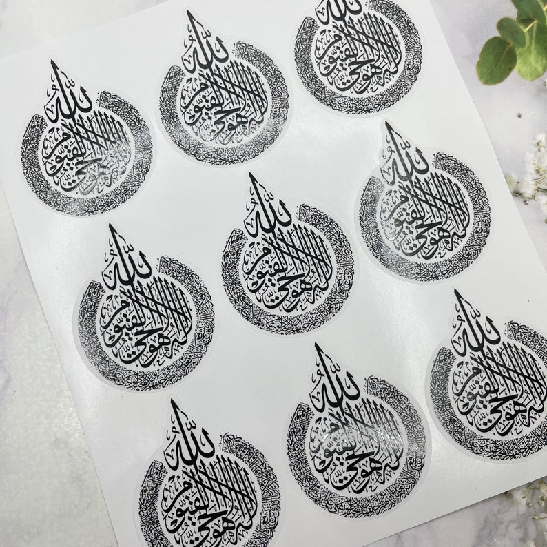May include: A sheet of clear stickers featuring black Arabic calligraphy. Each sticker has a teardrop shape with intricate text and a decorative border. The stickers are arranged on a white background.