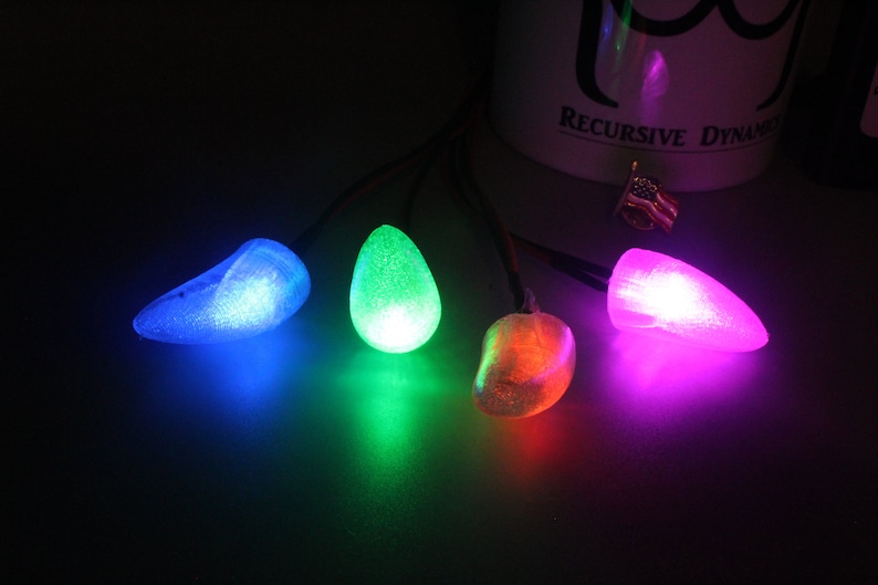 Pu&ograve; includere: Una stringa di quattro luci colorate e luminose. Le luci hanno la forma di gocce e emettono luce blu, verde, arancione e viola. Le luci sono collegate da fili sottili.