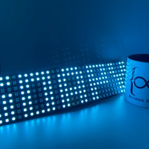 May include: A blue LED matrix display with a white mug that says "{∞} Recursive Dynamics" in black text.