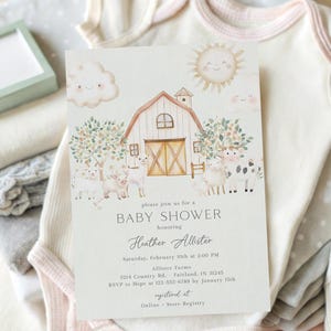 May include: A baby shower invitation with a barnyard theme, featuring a watercolor illustration of a barn, sheep, and a smiling sun. The invitation is surrounded by baby clothes in white, pink, and gray, along with a pair of white baby shoes.