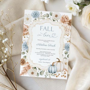 May include: An invitation card with the text "Fall in love" in a decorative frame, surrounded by floral and pumpkin illustrations in soft pastel colors. The card includes event details and is set against a backdrop of white flowers and a cream-colored fabric.