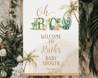 May include: A welcome sign for a baby shower with a jungle theme. The sign is white with brown text that says "Oh Boy! Welcome to Ruth's Baby Shower May 12th". The letters are decorated with green palm leaves, flowers, and dinosaurs.