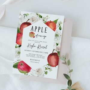 Może przedstawiać: Zaproszenie na baby shower z białym tłem i wzorem czerwonego jabłka. Zaproszenie zawiera napis "Apple of our eye" i imię "Kaylin Russel". Zaproszenie zawiera r&oacute;wnież datę i godzinę imprezy, miejsce oraz informacje o RSVP.