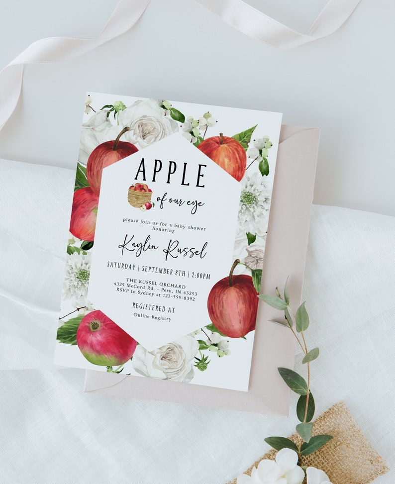 Może przedstawiać: Zaproszenie na baby shower z białym tłem i wzorem czerwonego jabłka. Zaproszenie zawiera napis "Apple of our eye" i imię "Kaylin Russel". Zaproszenie zawiera r&oacute;wnież datę i godzinę imprezy, miejsce oraz informacje o RSVP.