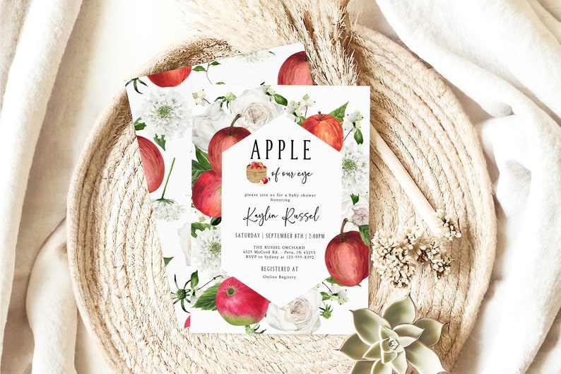 Może przedstawiać: Białe zaproszenie na baby shower z akwarelową ilustracją czerwonych jabłek, białych kwiat&oacute;w i zielonych liści. Tekst brzmi "APPLE of our eye" i "Kaylin Russel".