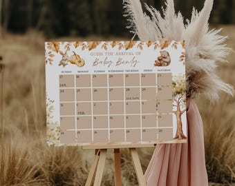 May include: A wooden easel displays a calendar-style sign with the text "GUESS THE ARRIVAL OF Baby Benly." The sign features illustrations of a rabbit, pumpkins, and a bear. The calendar grid is tan with dates from January and February.