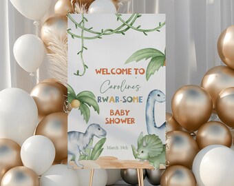 Könnte beinhalten: Willkommen zur RWAR-SOME Babyparty von Caroline Schild mit einem grünen, blauen und orangefarbenen Dinosaurier-Design. Das Schild steht auf einem Holzständer und ist von weißen und goldenen Luftballons umgeben.